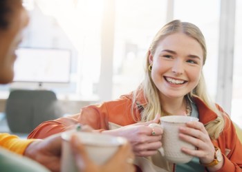 Coffee, friends and women in conversation in home on sofa, bonding or having fun together. Happy, girls talking and tea in lounge, smile and people drink espresso in living room of interracial house happiness