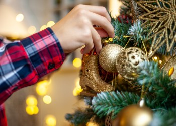 The hands of a young man decorate the Christmas tree with white balls. Preparing for Christmas. Close-up. A branch of a snow-covered Christmas tree with white and gold decorations.